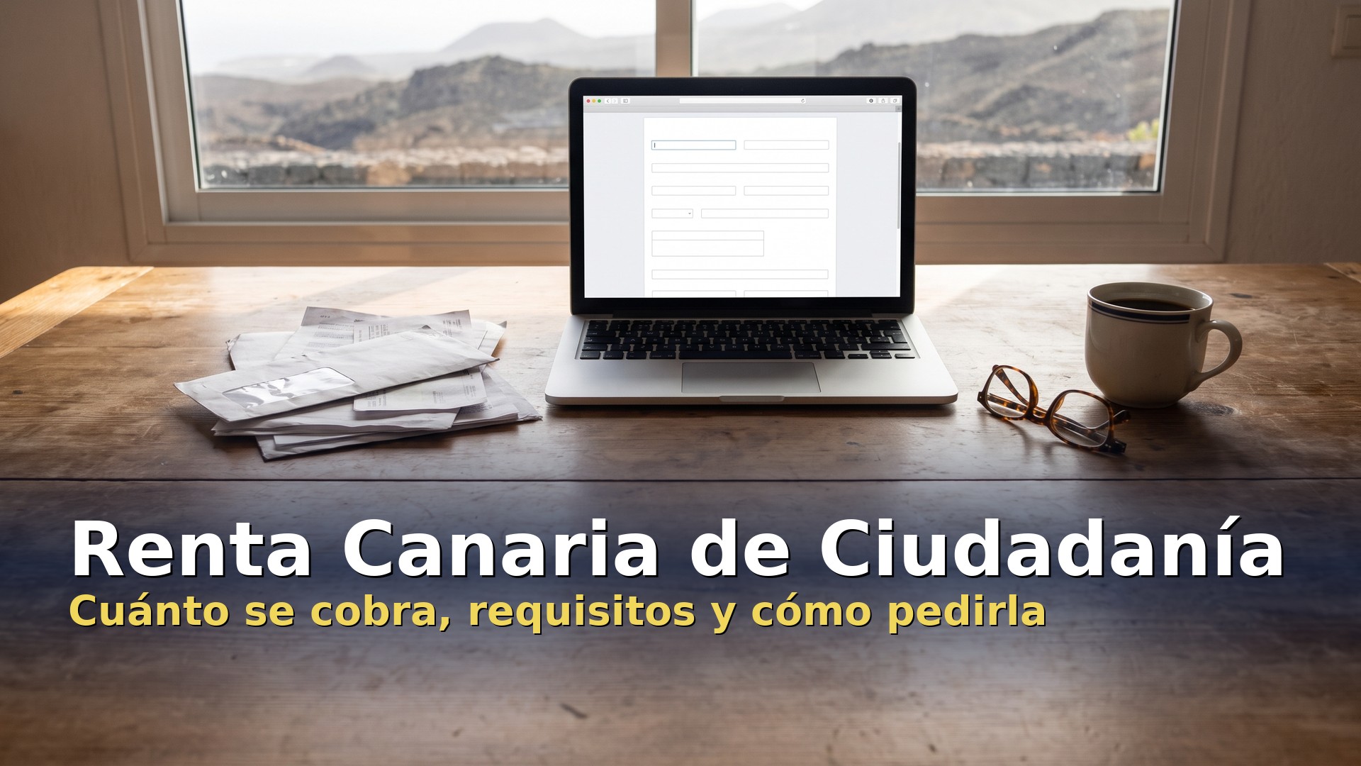 Renta Canaria de Ciudadanía: facturas, portátil con un formulario y gafas sobre una mesa con vistas a montes volcánicos